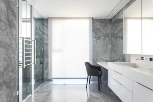 Modern minimalist bathroom with marble walls and floor, glass shower enclosure, and white vanity.
