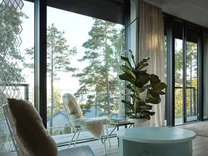 A minimalist living room featuring large glass windows overlooking a forested area.