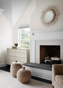 A minimalist white living room with a fireplace, dresser, and abstract sculptures.