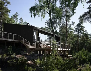 A modern, black-clad house surrounded by tall trees.