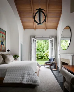 A modern bedroom with white painted walls, wooden flooring, and a large window leading to a garden.