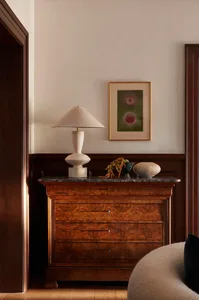 A modern console with a marble top displaying a lamp, vase, and plant.