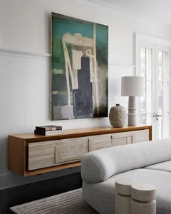 A modern floating console table with a large abstract painting above, minimalistic white sofa, and a lamp.