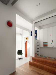 A minimalist kids playarea with a wooden floor, white walls, and colorful plastic balls in a shallow pool.