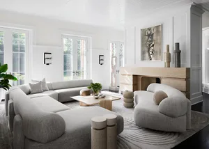A spacious, minimalist living room with white walls, a large modern sofa, and a wood-burning fireplace.
