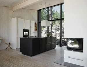 A modern residential kitchen with white cabinets, black countertops, and a large window overlooking a natural landscape.