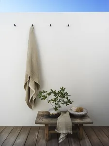 Minimalist bathroom scene with a ceramic plant on a wooden bench, a textured towel hanging on the wall, and a wood and cerami