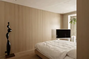 A minimalist bedroom with white wooden walls and a black abstract sculpture, featuring a bed with white sheets and a televisi