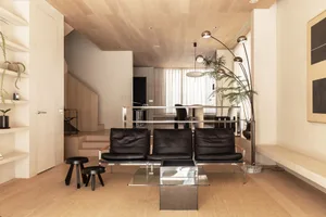 Modern minimalist living room featuring wood-paneled walls, black leather sofas, glass coffee table, and potted plants.
