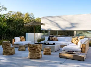 An outdoor residential patio featuring minimalist furniture, including a white sectional sofa, woven rattan chairs, and a woo