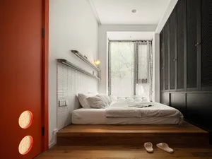 A modern bedroom with a white bed, wooden flooring, and a large window