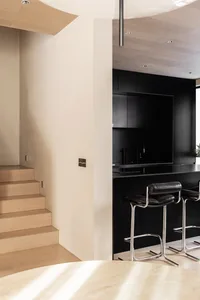 A modern kitchen with black cabinets, a wooden staircase, and a white ceiling.