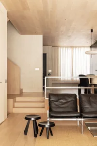 A modern living room with a black leather sofa on a wooden floor, featuring minimalist design elements and neutral colors.
