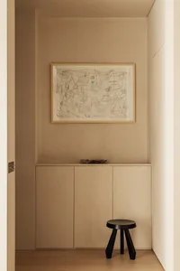 A minimalist entryway featuring neutral-toned cabinets and a black stool.
