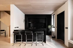 Modern industrial kitchen interior with dark wood cabinetry, black countertops, and 3 black bar stools.