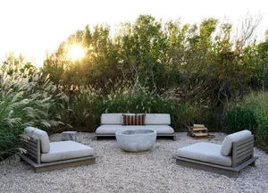 A modern outdoor living space featuring a concrete fire pit surrounded by gravel and pampas grass.