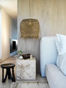 A textured lamp shade hanging above a white sofa, placed on a concrete side table with various decorative items such as a whi