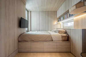 A minimalist bedroom featuring wooden elements and a built-in bed with storage drawers beneath.
