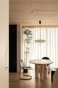 Modern minimalist dining room with wooden flooring, a round table, black chairs, and sheer curtains hanging from the ceiling.