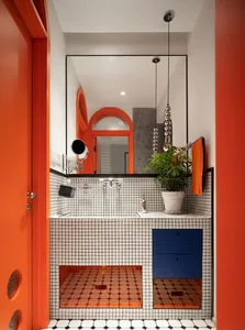 A modern bathroom featuring orange-tiled walls and a white counter with a blue drawer.