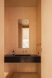 A modern bathroom with a wooden finish, featuring a black countertop and a rectangular mirror above the sink.