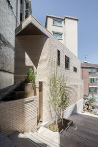 A modern building constructed with brick, featuring a unique facade and a small tree in a flower bed.