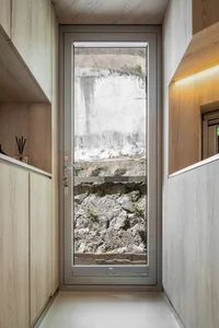 A modern interior doorway with metal and glass elements, revealing a view of concrete and rocky terrain outside.