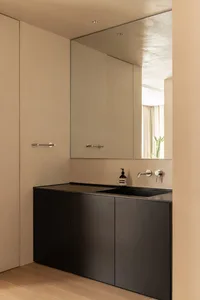 Modern minimalist bathroom interior featuring sleek black cabinets, a large mirror, and a concrete countertop.