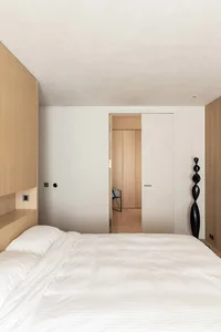 A minimalist bedroom with a bed, wall-mounted shelves, and a black sculpture.