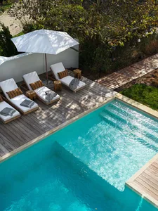 A modern pool deck with wooden deck, glass enclosure, and white lounge chairs.
