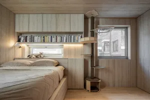 A minimalist bedroom with wooden elements and a cat perched on a shelf.