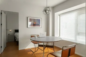 A minimalist home office with a white steel dining table and brown leather chairs.