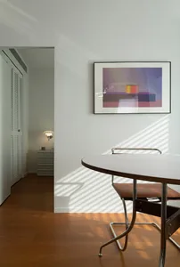 A modern residential room featuring white furniture, a round table, and a framed abstract art piece.
