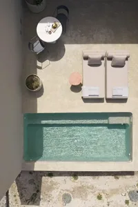Minimalist outdoor area with a concrete pool, lounge chairs, and dining table.