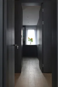 A modern, minimalist corridor with black walls and a wooden floor, showcasing sleek doors and a window with sunflowers.