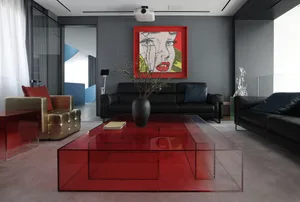 Modern living room with a clear red glass coffee table, black leather sofa, and a black and red abstract painting on the wall