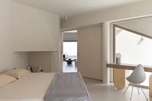 A minimalist bedroom with white furniture and a grey bedspread.