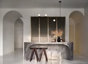 An industrial-style interior with concrete stools and a vase with dry plants on a textured concrete surface.