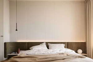 A minimalist bedroom with a brown upholstered bed, concrete textured wall, and white bedding on a wooden floor.