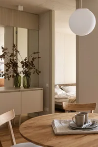 Modern minimalist residential interior featuring wooden table, concrete walls, and glass vase with dried leaves.