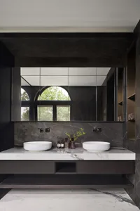 A modern bathroom with a marble countertop and vanity, featuring a large mirror and a window with green trees outside.