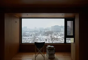 一間現代客廳，鋪設木質地板，並設有大型玻璃窗，可俯瞰雪景城市景觀。
