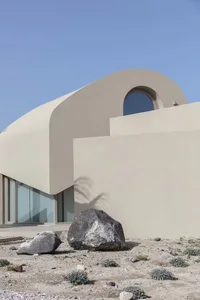 Modern building with a curved, concrete exterior featuring a circular window and a palm tree shadow on the wall.