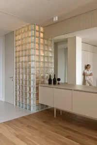 A modern interior featuring glass blocks and concrete furniture, with a woman leaning against a wall.