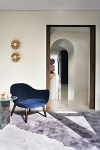 Modern interior featuring a blue upholstered armchair with wooden legs, next to a glass-top coffee table, and a wall with two