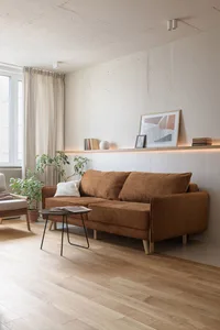 A modern living room featuring a brown sofa, wood panels, and green plants, with a picture on the wall.