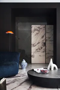 A modern living room featuring a dark marble coffee table with a bowl of fruit, an abstract white sculpture, and a blue uphol