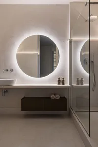 Modern minimalist bathroom with circular mirror featuring backlighting and concrete floor and walls, providing a sleek and co