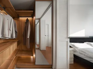 A modern minimalist bedroom featuring white walls and wooden flooring, with a bed and wardrobe.
