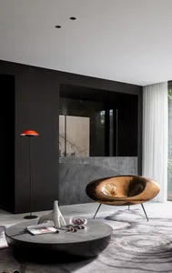 Modern minimalist living room with a bronze sculptural chair, low round table, and red floor lamp on a patterned rug with a b